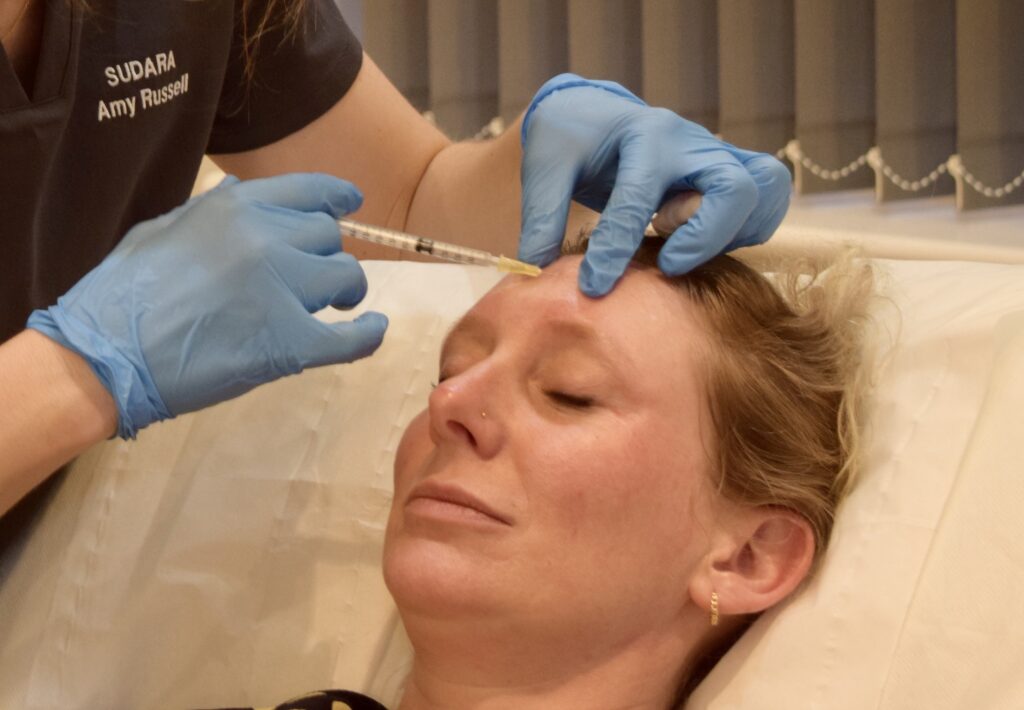 A woman receiving a cosmetic injection while lying down, with a practitioner administering the treatment.