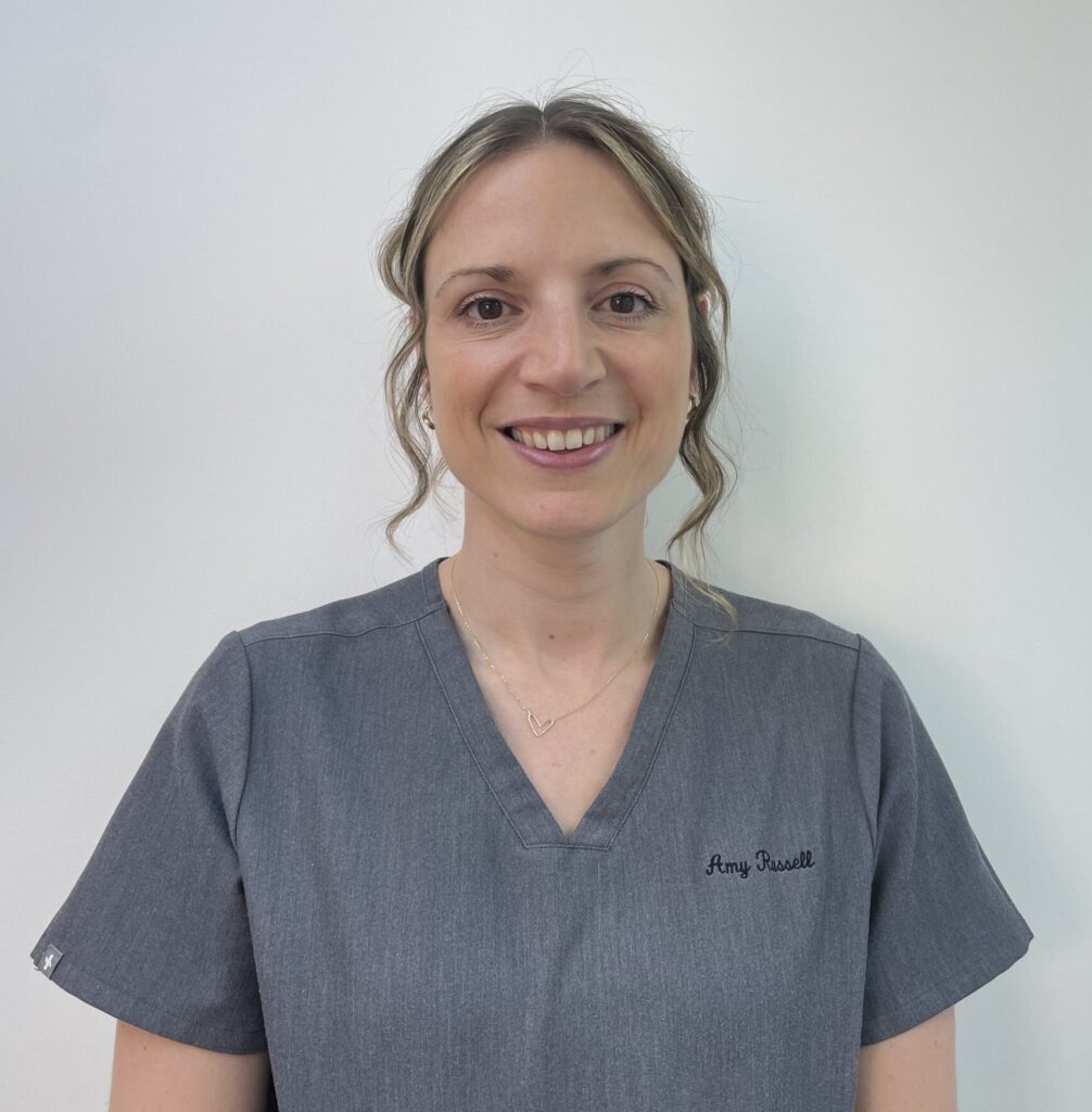 A smiling woman in a gray scrubs top stands against a plain background.